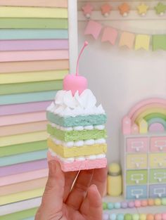 a person holding up a piece of cake with a cherry on top in front of a rainbow colored wall