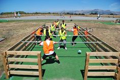 a group of people in orange vests playing soccer on a green field with wooden benches