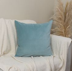 a blue pillow sitting on top of a white couch next to a tall grass plant