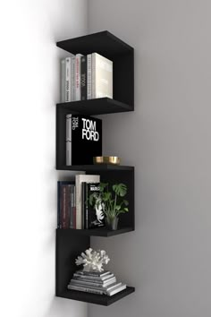 three black shelves with books on them against a white wall in the corner of a room