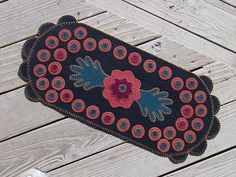 a black rug with red and blue flowers on it sitting on a wooden floor next to a pair of white shoes