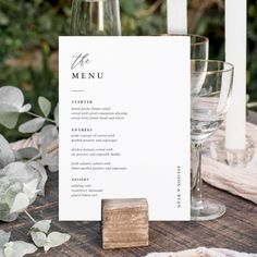 a menu sitting on top of a wooden table next to two wine glasses and a candle