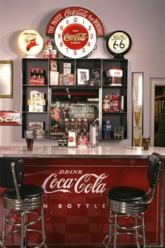 two stools at the bar with coca - cola signs on the wall behind them