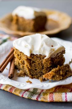 a slice of carrot cake with cream cheese frosting and cinnamon sticks on a plate