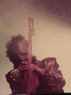 a man holding a guitar in his right hand while wearing a shiny jacket and tie