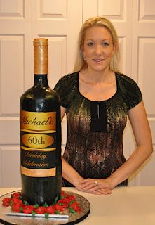 a woman standing next to a bottle of wine on top of a cake covered in flowers