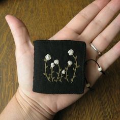 a hand holding a small black square with white flowers on it