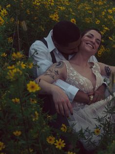 a bride and groom cuddle in a field of wildflowers