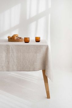 an empty table with two cups on it and bread in front of the tablecloth