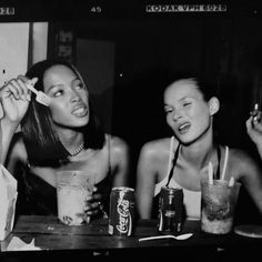 two women sitting at a table with drinks and sodas in front of their faces