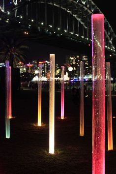 illuminated columns in front of the sydney harbour bridge at night with city lights behind them