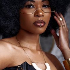 a woman with an afro wearing glasses and a gold choker is posing for the camera