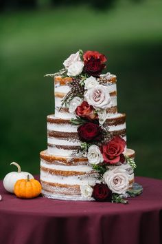 a multi layer cake with flowers on top sitting on a table next to a pumpkin