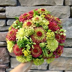 a hand holding a bouquet of flowers in front of a brick wall and stone wall