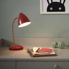 a desk lamp sitting on top of a white counter next to a book and phone