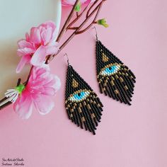 a pair of black beaded earrings sitting on top of a pink table next to flowers