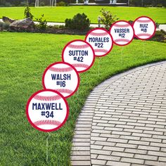 four baseball yard markers with names and numbers on them in front of a brick path