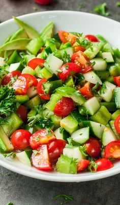 a white bowl filled with cucumber, tomato and avocado salad on top of a table