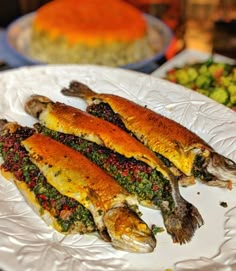 three fish on a white plate next to other foods