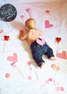 a baby laying on top of a bed next to a heart shaped pinata and a black balloon