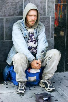 a man sitting on the ground next to a skateboard with his hands in his pockets