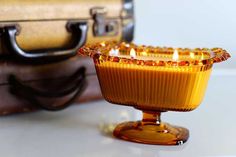 an orange glass candle holder sitting on top of a table next to a suit case