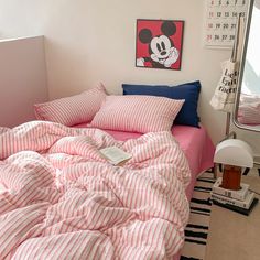 a bed with pink and white striped comforter next to a mirror in a bedroom