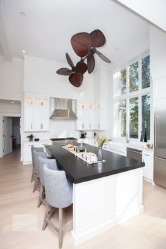 a large kitchen with an island and ceiling fan in the center, surrounded by white cabinets