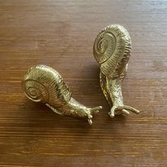 two small brass snails sitting on top of a wooden table