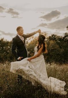 a bride and groom standing in tall grass with the sun shining through the clouds behind them