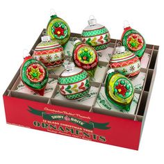 twelve christmas ornaments in a red box with green and white designs on the top, including poinsettis