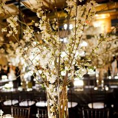 a tall vase filled with white flowers sitting on top of a table covered in tables cloths