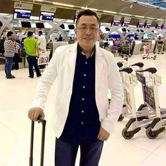 a man in a white jacket and glasses holding a suitcase at an airport baggage claim