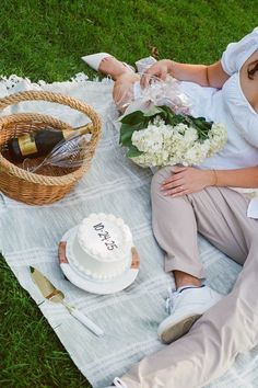 a man and woman are sitting on the grass with their wedding cake in front of them