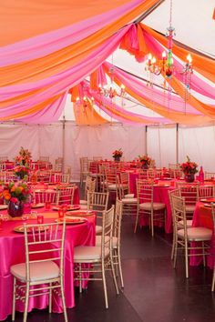 the inside of a tent with tables and chairs covered in pink and orange cloths