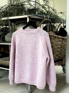 a pink sweater is hanging on a rack in front of a basket full of plants