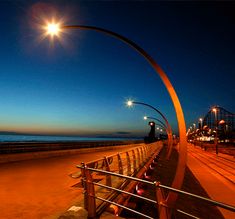 the sun shines brightly on an empty beachfront at night, with benches lined up along the boardwalk