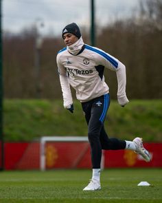 a man running on a soccer field with a ball in his hand and wearing a hat