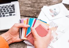 a person is holding some color samples in front of a laptop and other office supplies