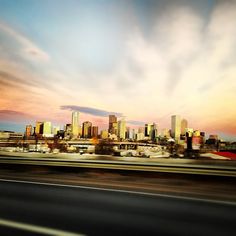 the city skyline is seen from across the highway at sunset or dawn with clouds in the sky