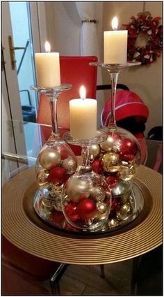 two wine glasses filled with ornaments on top of a glass table topped with candles and christmas balls