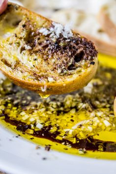 a spoonful of olive oil being used to scoop some bread into a bowl with pesto on it