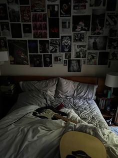 a guitar laying on top of a bed next to a wall full of pictures and posters