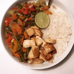 a white plate topped with rice and veggies next to a slice of lime