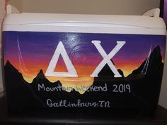 a cooler with the word mountain weekend written on it and mountains in the background at sunset