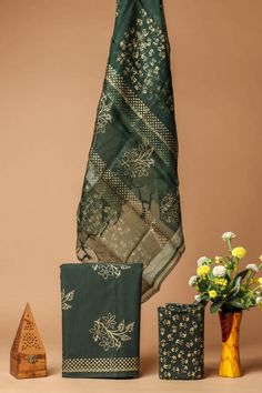 two vases with flowers in them next to a green and gold sari cloth