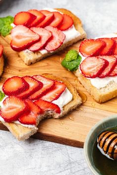 slices of toast with strawberries and cream cheese on them next to a bowl of honey