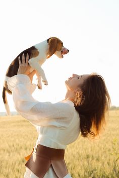 a woman holding a dog up in the air while standing on top of a field