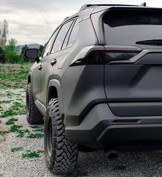 the rear end of a gray suv parked on gravel with grass growing all around it