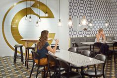 two women sitting at tables in a restaurant with patterned wallpaper and gold circles on the walls